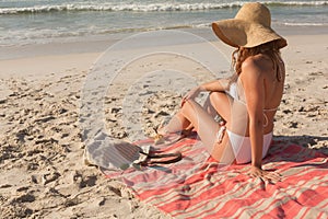 Young Caucasian woman in hat and bikini relaxing on the beach