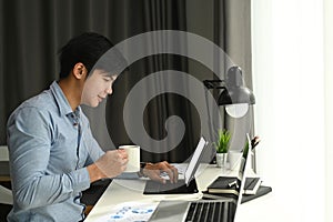 Side view of a graphic designer is working with computer tablet and drinking coffee at his workspace.