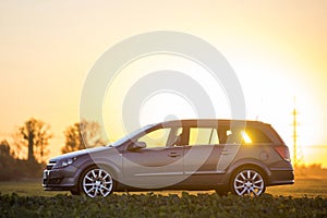Side view of gray silver empty car parked in countryside on blurred rural landscape and bright orange clear sky at sunset copy
