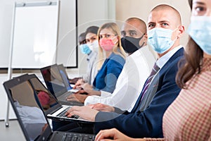 Side view of a group of businessmen in protective masks undergoing training under the guidance of teacher