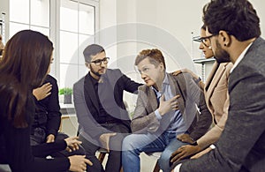 Side view on group of gathered people, comforting their comrade by putting their hand on his shoulder.