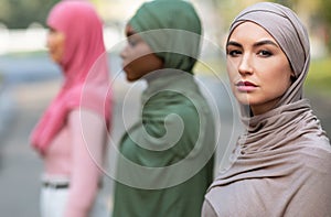 Side-View Group Portrait Of Three Diverse Muslim Women Posing Outside