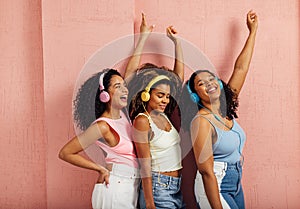 Side view of a group of young women raising hands up. Three females wearing headphones while standing against a pink wall