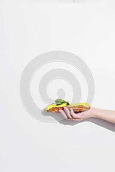 Side view of a hand with traditional french eclair in it over white background with copy space.