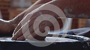 Side view of hands work on pottery wheel, shaping a clay pot