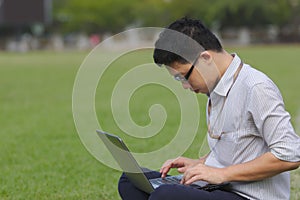Side view of handsome Asian business man working with laptop on the green grass.