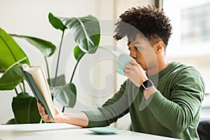 Side view of handsome black guy reading book at cafe