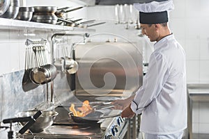 side view of handsome chef frying steak with fire
