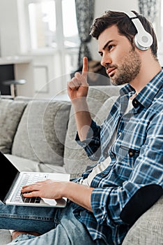 Side view of handsome freelancer in headphones having idea while using laptop