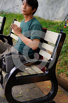 side view of a handsome man in green sitting on a park bench.