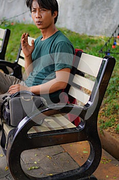 side view of a handsome man in green sitting on a park bench.