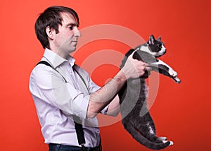 Handsome man in shirt with rolled sleeves holding cute gray and white cat and looking at it back