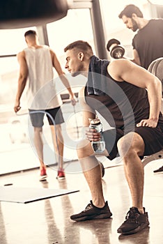 side view of handsome sportsmen resting and holding bottle of water