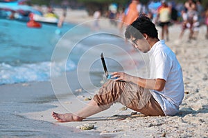 Side view of handsome young Asian man using laptop on the beach.