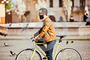 Side view of handsome young bearded man in sunglasses looking away while riding on his bicycle outdoors.