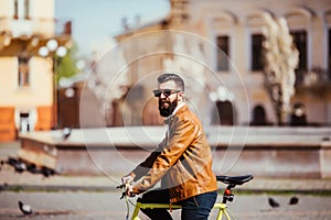 Side view of handsome young bearded man in sunglasses looking away while riding on his bicycle outdoors.