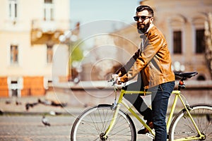 Side view of handsome young bearded man in sunglasses looking away while riding on his bicycle outdoors.