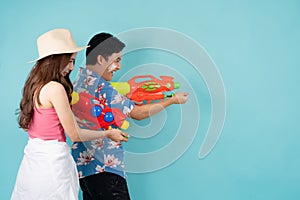 Side view of happy Asian couple in summer clothes with water guns on blue background, Songkran festival in Thailand