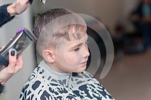 Side view of happy boy is sitting in barber salon with wet hair and cuts her hair