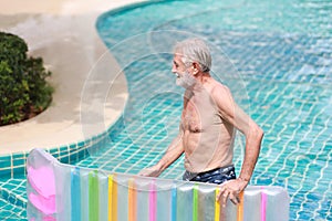Side view happy elderly caucasian swimming and playing rubber boat in swimming pool during retirement holiday with relaxation and
