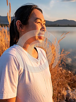 Side view of happy hopeful woman looking away to nature reflection on water at sunset lakeside