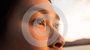 Side view of happy hopeful woman looking away to nature reflection on water at sunset lakeside. Close up of her eyes