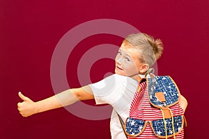 Side view Happy joyful schoolboy wearing backpack and giving thumbs up isolated on red wall