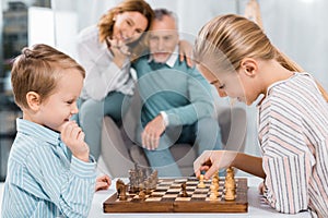 side view of happy kids playing chess while their grandparents sitting near