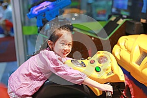 Side view of happy little Asian kid girl playing arcade video game. Motorcycle Racing