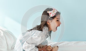Side view of happy little girl in pajama has an amazed expression afterwake up in the bed, isolated on light blue background. Kid