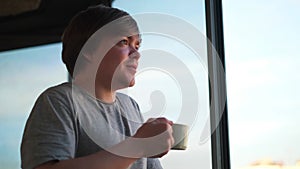 Side view of a happy man at home balcony relaxed and cheerful enjoying cup of coffee. Concept. Young smiling man looking