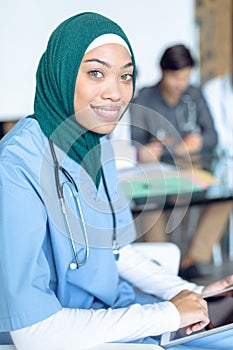 Happy female surgeon in hijab looking at camera while using digital tablet in the hospital