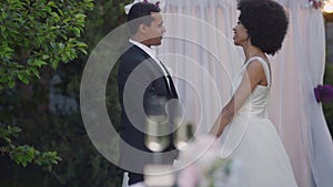 Side view of happy newlyweds holding hands talking and smiling standing at wedding altar. Joyful young beautiful bride