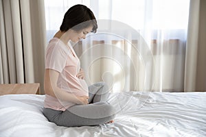 Side view happy pregnant woman caressing belly, relaxing in bedroom