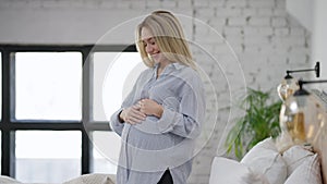 Side view of happy pregnant woman talking to unborn fetus caressing belly. Cheerful smiling beautiful blond Caucasian