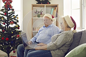 Side view of happy senior couple using laptop watching favorite Christmas movies.