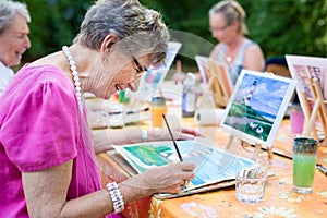 Side view of a happy senior woman smiling while drawing as a recreational activity or therapy outdoors together with the group.