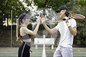Side view of happy, smiling male and female tennis players high-fiving each other after playing a good match.