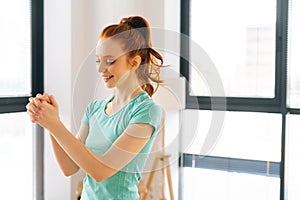 Side view of happy sporty young woman doing stretching exercise wrist before fitness training at home office near window