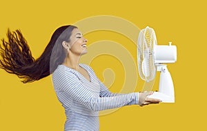 Side view of happy woman holding electric fan and enjoying fresh air blowing in her face