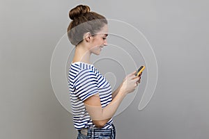 Side view of happy woman reading message on smartphone, smiling, using mobile device, browsing web.