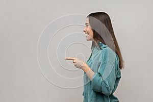 Side view of happy young adult woman standing, pointing and showing copyspace with happy face.