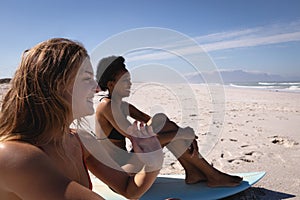 Happy young women sitting on surfboard at beach in the sunshine