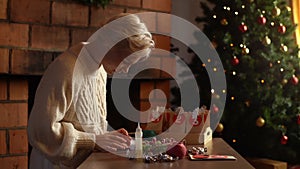 Side view of happy young woman making paper bags from kraft paper for advent calendar on Christmas Eve sitting at table