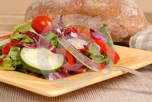 Side view of a healthy salad on a yellow plate with rustic bread