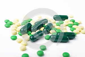 A side view of a heap of yellow and green medicine pills and capsules.