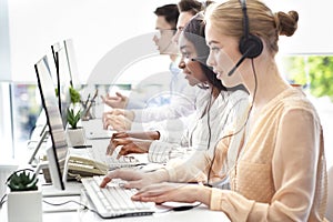 Side view of helpline operators with headsets consulting customers at modern call center, empty space