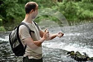 Side view of a hiker in a shirt with a backpack near the river spraying insect repellent on skin