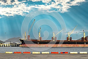 Side view of a huge bulk cargo ship docking at harbor discharging steel cargo with a beautiful sky background.