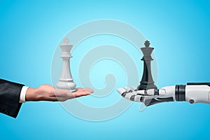 Side view of human hand holding white chess king and android robot hand holding black chess king opposite one another on